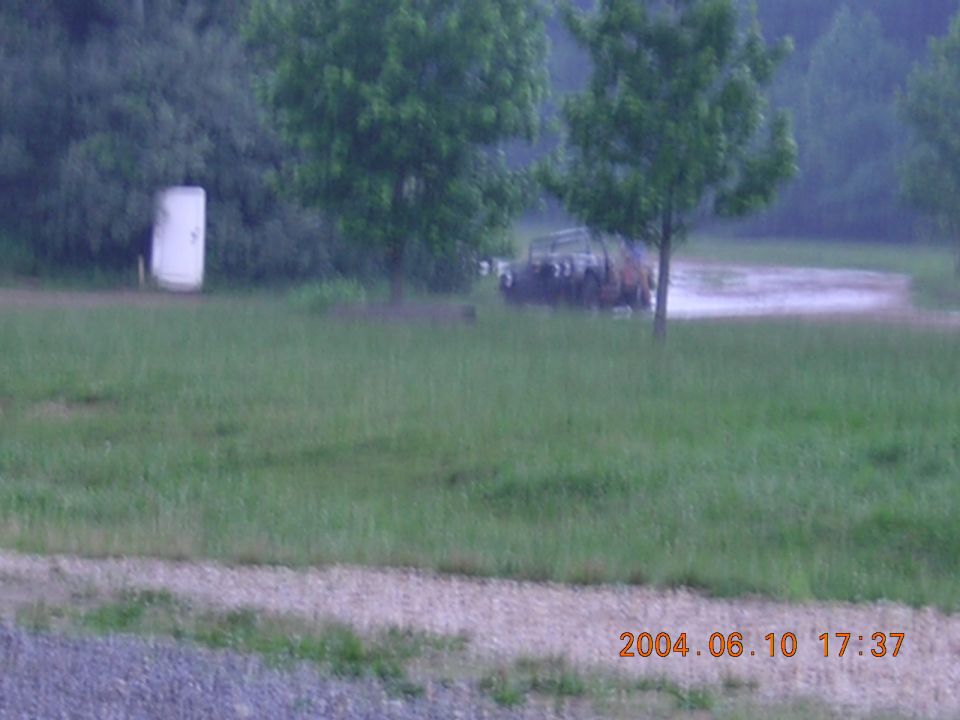Old truck parked in a grassy field with trees and a white silo in the background