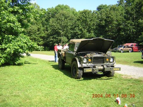 1984 Chevrolet Blazer - A military truck with its hood up is parked on a grassy area next to a gravel path, with other vehicles in the background.