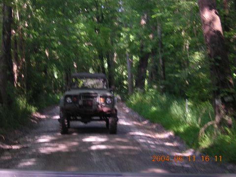 1984 Chevrolet Blazer - An olive green off-road vehicle drives down a tree-lined dirt road.