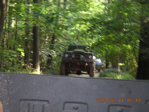 1984 Chevrolet Blazer - A muddy off-road vehicle navigates a wooded trail, seen from the perspective of another vehicle.