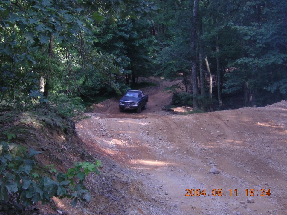 Dark blue pickup truck driving on a dirt road in a wooded area