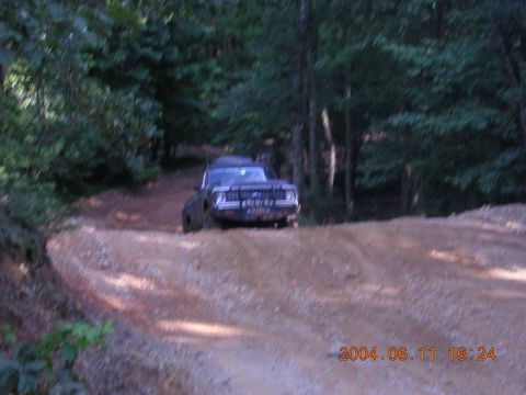1984 Chevrolet Blazer - A dark SUV navigates a rough dirt road surrounded by trees.