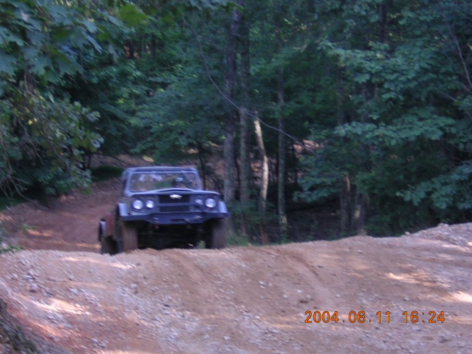 Dark off-road vehicle on dirt path. Visible timestamp and website logo