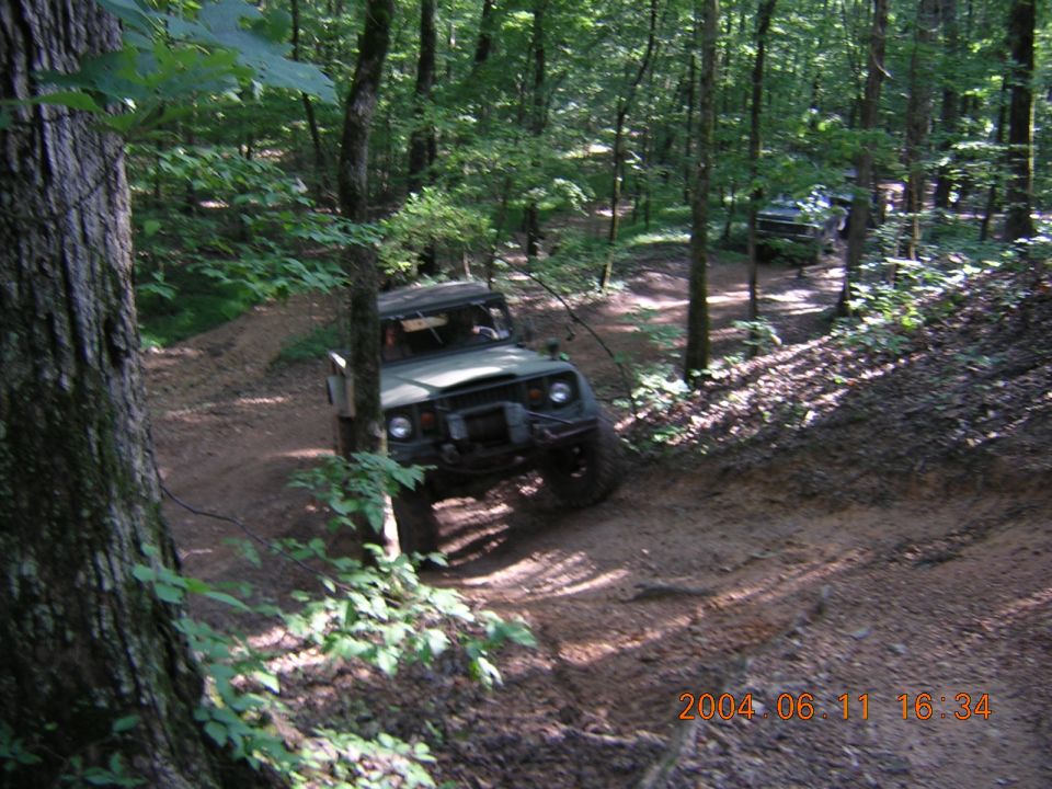 Olive green off-road vehicle on a dirt path in a forest, front-left 3/4 view