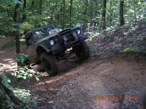 1984 Chevrolet Blazer - An olive green off-road vehicle navigates a steep dirt path in a wooded area.