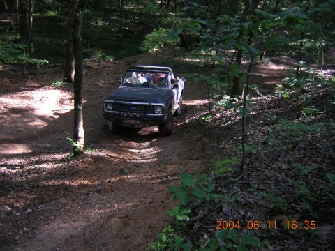 1984 Chevrolet Blazer - Off-road truck navigates a wooded trail, kicking up dust.