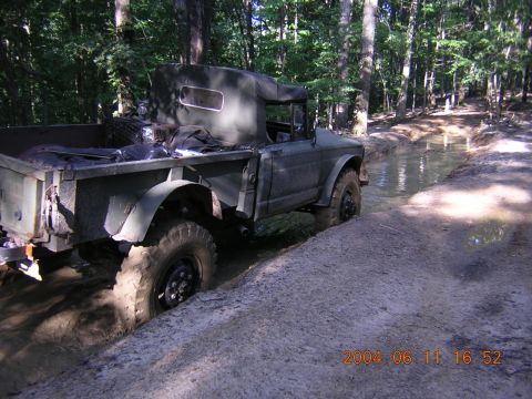 1984 Chevrolet Blazer - This olive drab truck is navigating a challenging muddy path through a wooded area.