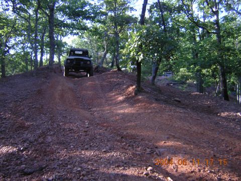 1984 Chevrolet Blazer - An off-road vehicle navigates a steep, rutted dirt path surrounded by trees. Another vehicle is parked in the distance.