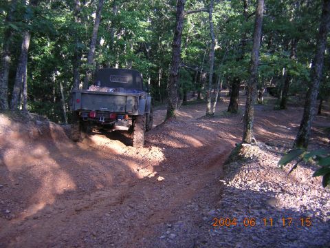 1984 Chevrolet Blazer - A military-style truck navigates a wooded trail, kicking up dust as it goes.