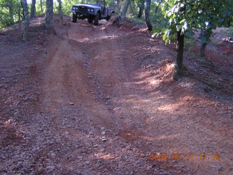 1984 Chevrolet Blazer - A dark off-road vehicle navigates a steep, rocky incline in a wooded area.
