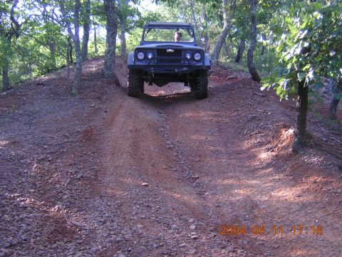 1984 Chevrolet Blazer - A dark-colored off-road vehicle navigates a steep, rutted dirt path through a wooded area.