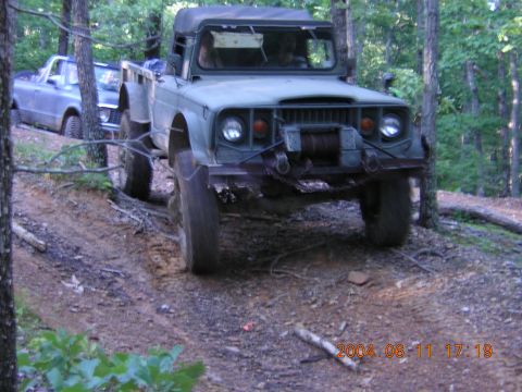 1984 Chevrolet Blazer - An olive green off-road vehicle navigates a wooded trail, with another vehicle visible behind it.