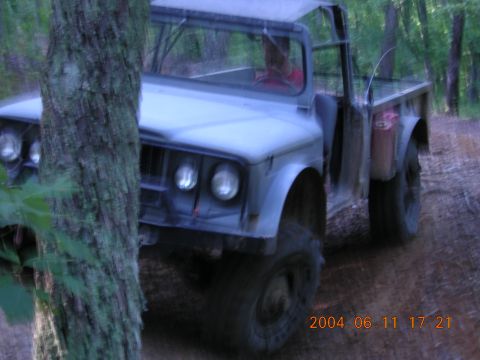 1984 Chevrolet Blazer - A light blue off-road truck with a soft top is seen on a dirt path, partially obscured by trees.