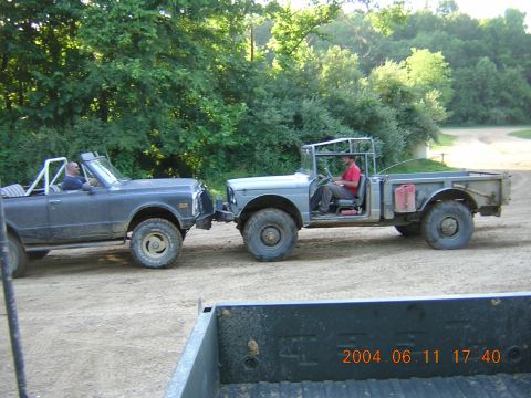 1984 Chevrolet Blazer - Two off-road vehicles are connected on a dirt road, with trees in the background.