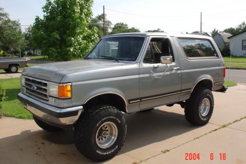 1987 Ford Bronco - This lifted Ford Bronco is parked on a concrete driveway with a residential area in the background.
