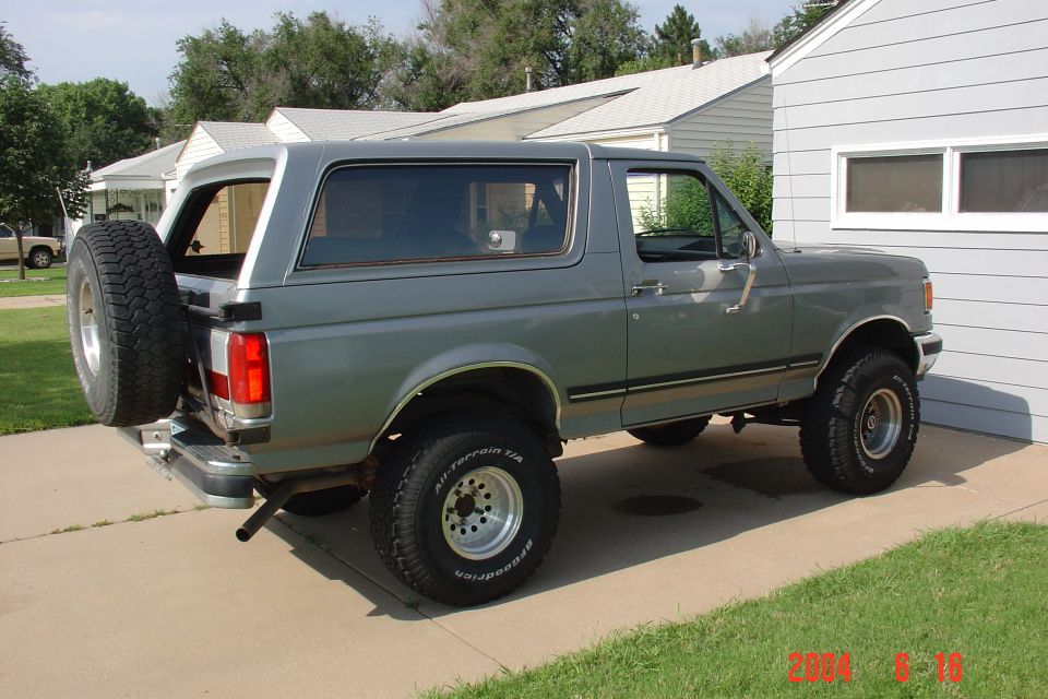 Gray 1987 Ford Bronco parked in a driveway, rear-mounted spare tire, 3/4 front view