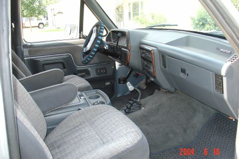 1987 Ford Bronco - The interior of a Ford Bronco is shown, cloth seats and a dashboard with wood trim accents.