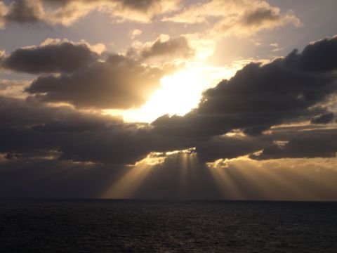 1995 Ford Bronco - Sunbeams pierce through dark clouds over a calm ocean during sunset.