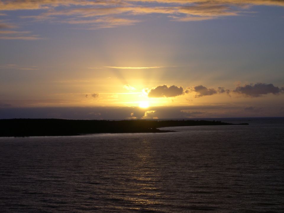 Sunset over the ocean with clouds and a dark landmass