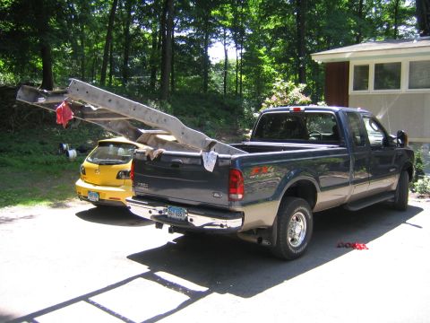 1978 Ford Bronco - Rear three-quarter view of a two-tone dark green and tan Ford F-250 FX4 Off Road extended cab in a wooded driveway, hauling a long bare ste…
