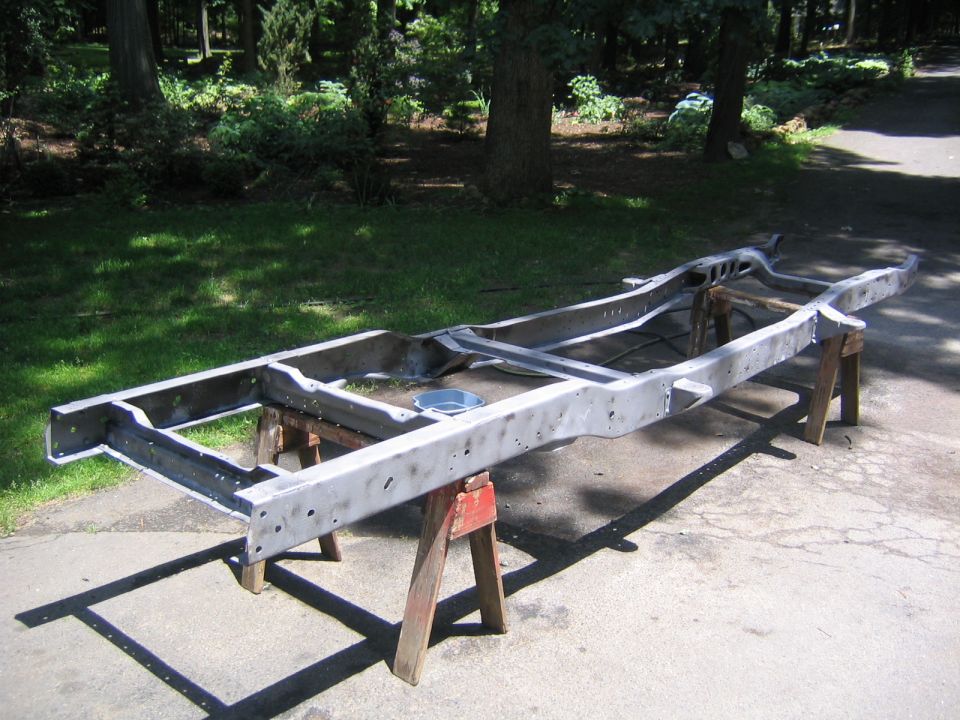 Bare stripped truck frame resting upside-down on wooden sawhorses in a driveway