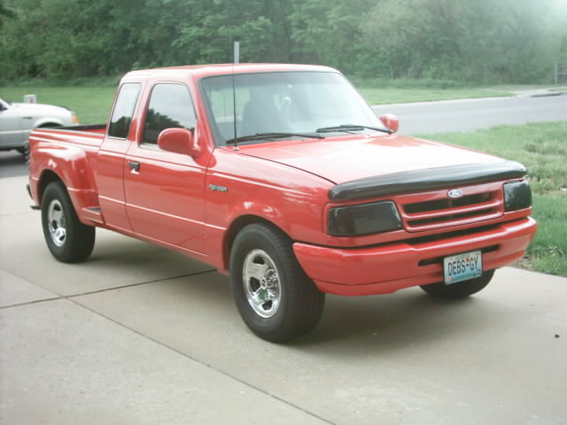 Red Ford Ranger extended-cab pickup with tinted headlights and hood deflector, parked on a driveway, front 3/4 view