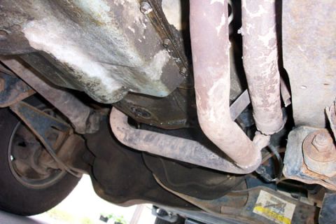 1995 Ford Bronco - Underside view of a vehicle showing exhaust piping, a metal fuel or transmission pan, and surrounding suspension and frame components, all…