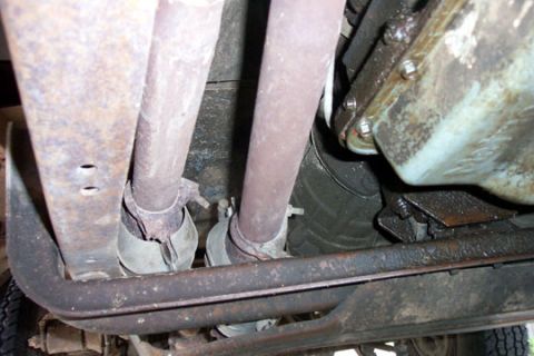 1995 Ford Bronco - Underbody view of two weathered exhaust pipes running side by side past a rusty rear crossmember, each secured with U-clamps where they end…