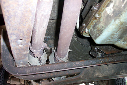 Dual exhaust pipes with U-clamps ending at a rusty crossmember, viewed from under the truck