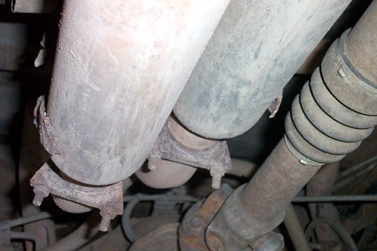 Under-vehicle view of dual mufflers with rusty U-bolt clamps next to the driveshaft