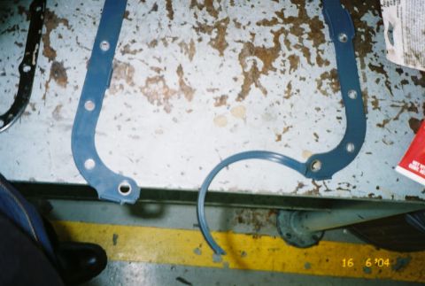 1988 Ford Bronco - A blue gasket lies on a stained workbench, with a bent section visible.