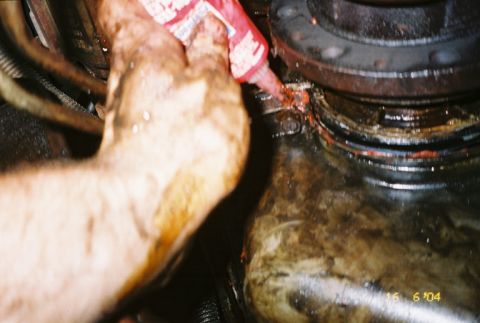 1988 Ford Bronco - A mechanic applies sealant to a greasy engine part, suggesting maintenance or repair work.