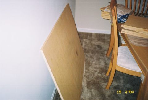 1988 Ford Bronco - A large sheet of plywood is propped against a wall in a room with carpet and furniture.
