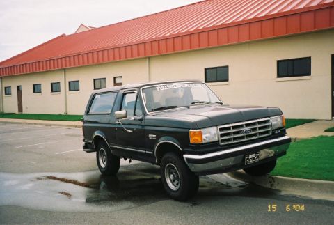 1988 Ford Bronco - This dark SUV, likely a 1987 model, is parked in front of a building with a red roof.