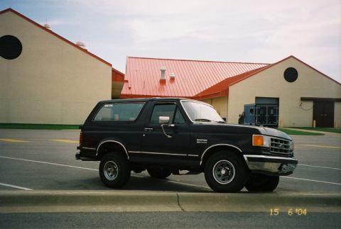 1988 Ford Bronco - A dark blue 1988 Ford Bronco is parked in front of a building with a red roof.