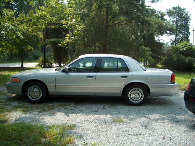 Silver 2000 Ford Crown Victoria parked on a gravel driveway with trees in the background