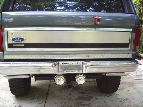 1986 Ford Bronco - Straight-on rear view of a dark green full-size Ford Bronco tailgate with a brushed trim panel, blue Ford oval, 'Electronic Fuel Injection'…