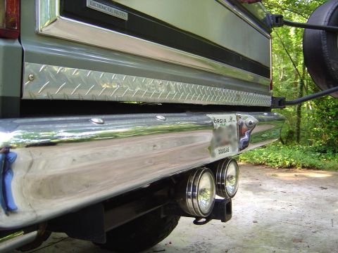 1986 Ford Bronco - Low-angle close-up of the rear of a green full-size SUV showing the chrome rear bumper, diamond-plate tailgate protector strip and an 'ELEC…