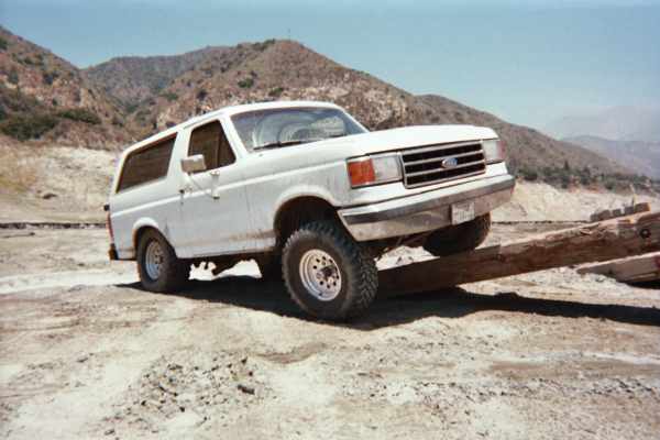 White full-size Ford Bronco with front wheel up on a log obstacle