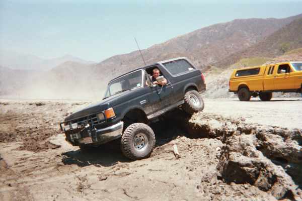 Black SUV climbing a dirt mound with driver leaning out the window