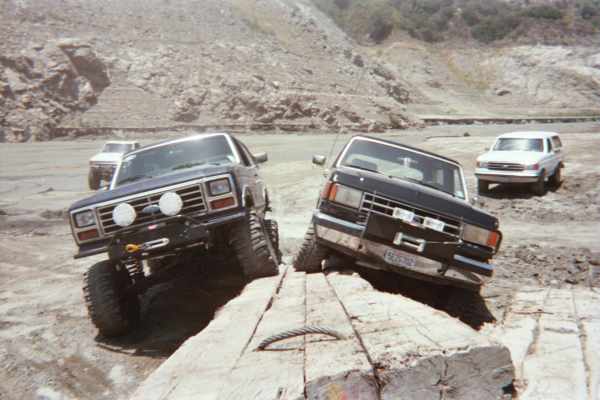 Two lifted SUVs front-to-camera straddling a concrete block in a quarry