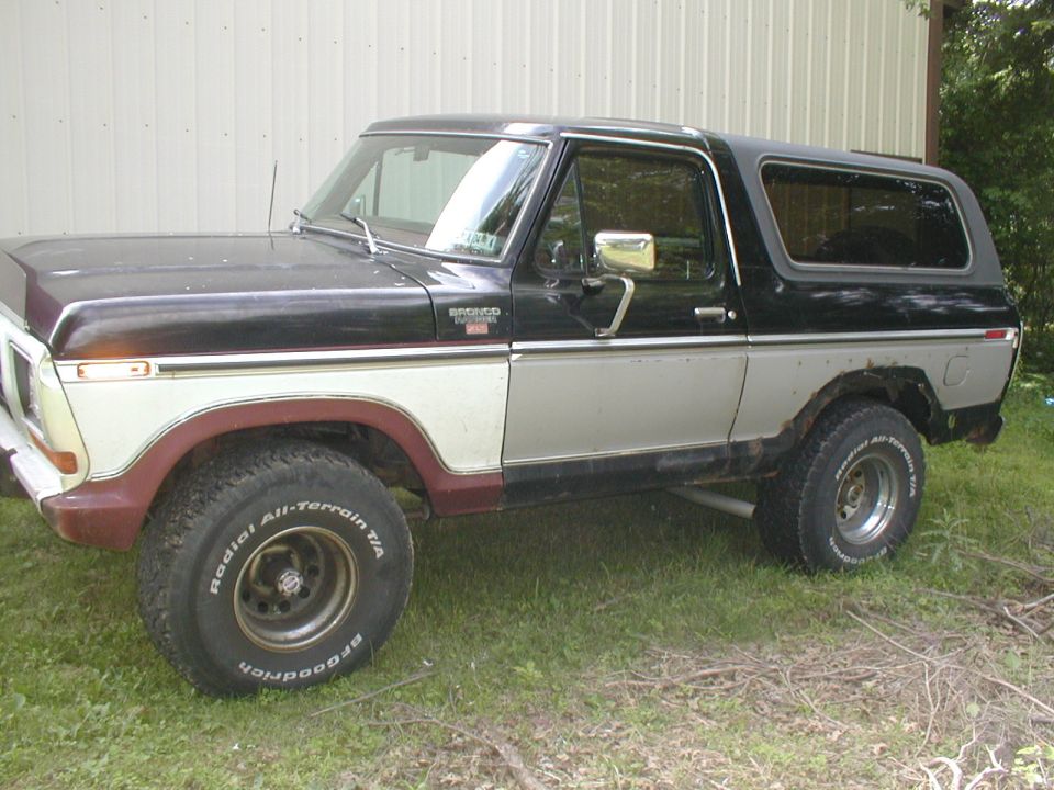 Black and silver two-door Ford Bronco with maroon fender flares, parked on grass