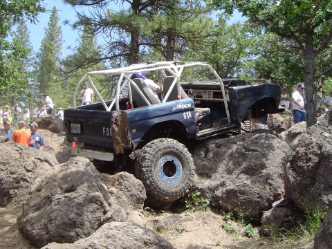 1989 Ford Bronco - This modified Ford Bronco is tackling a challenging off-road course with spectators watching.