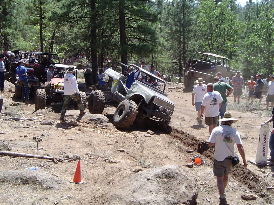 Several rock buggies and spectators working a rutted dirt obstacle at an off-road competition