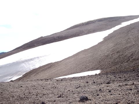 1996 Ford Bronco - A vast, barren landscape dominated by a rocky slope and scattered snowfields under a bright sky.