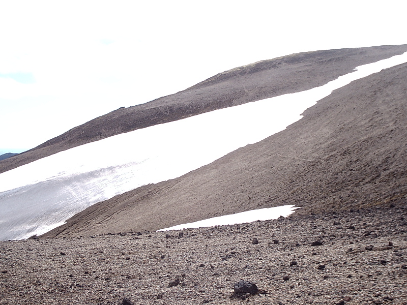 Snow patches on a barren gravel mountain slope under overcast sky