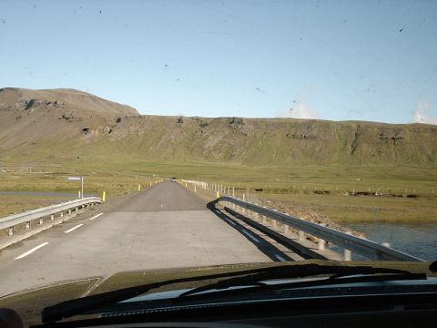 1996 Ford Bronco - View from inside a vehicle driving on a road through a scenic rural landscape with mountains in the background.