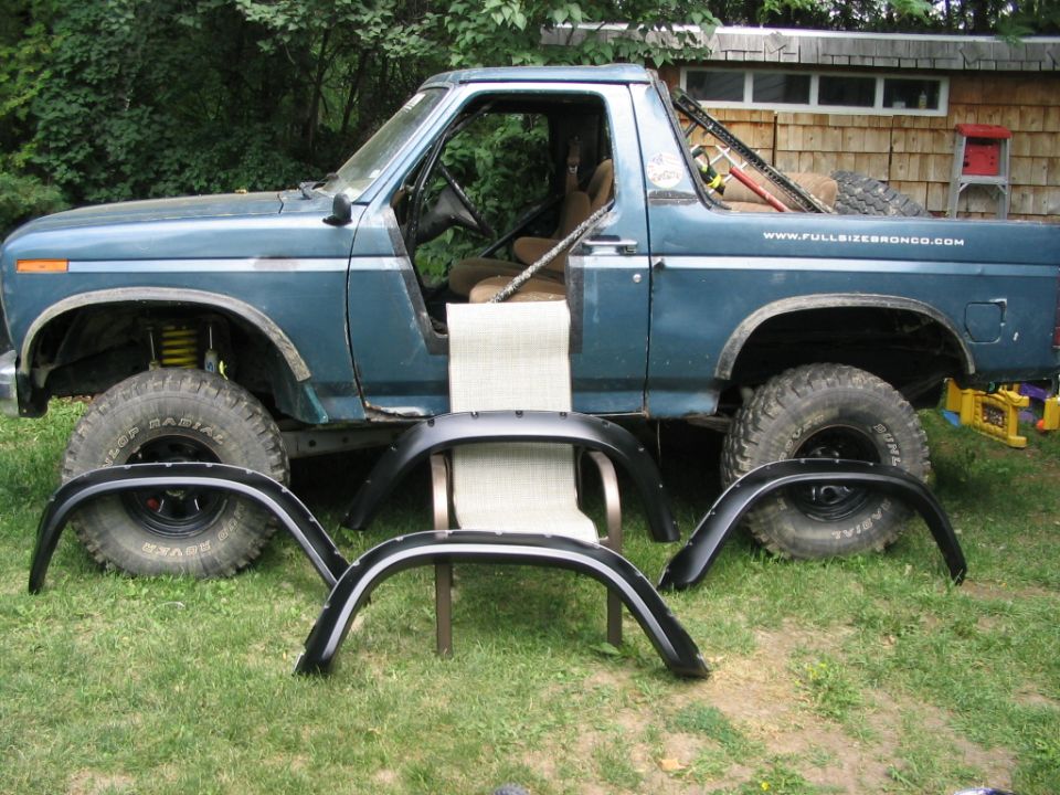 Blue Ford Bronco with top removed in a yard surrounded by fender flares and a lawn chair