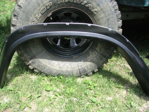 1986 Ford Bronco - A fender flare is placed in front of a large off-road tire. Text on the tire reads 'Mud Rover'.