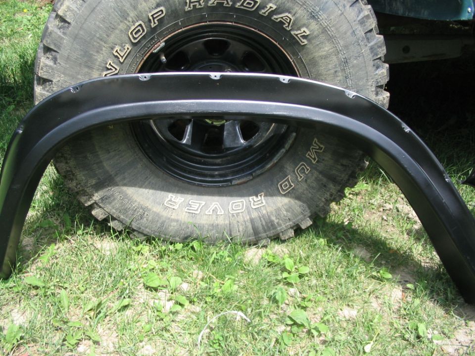 Close-up of a large off-road tire with 'Mud Rover' text and a black fender flare resting in front of it